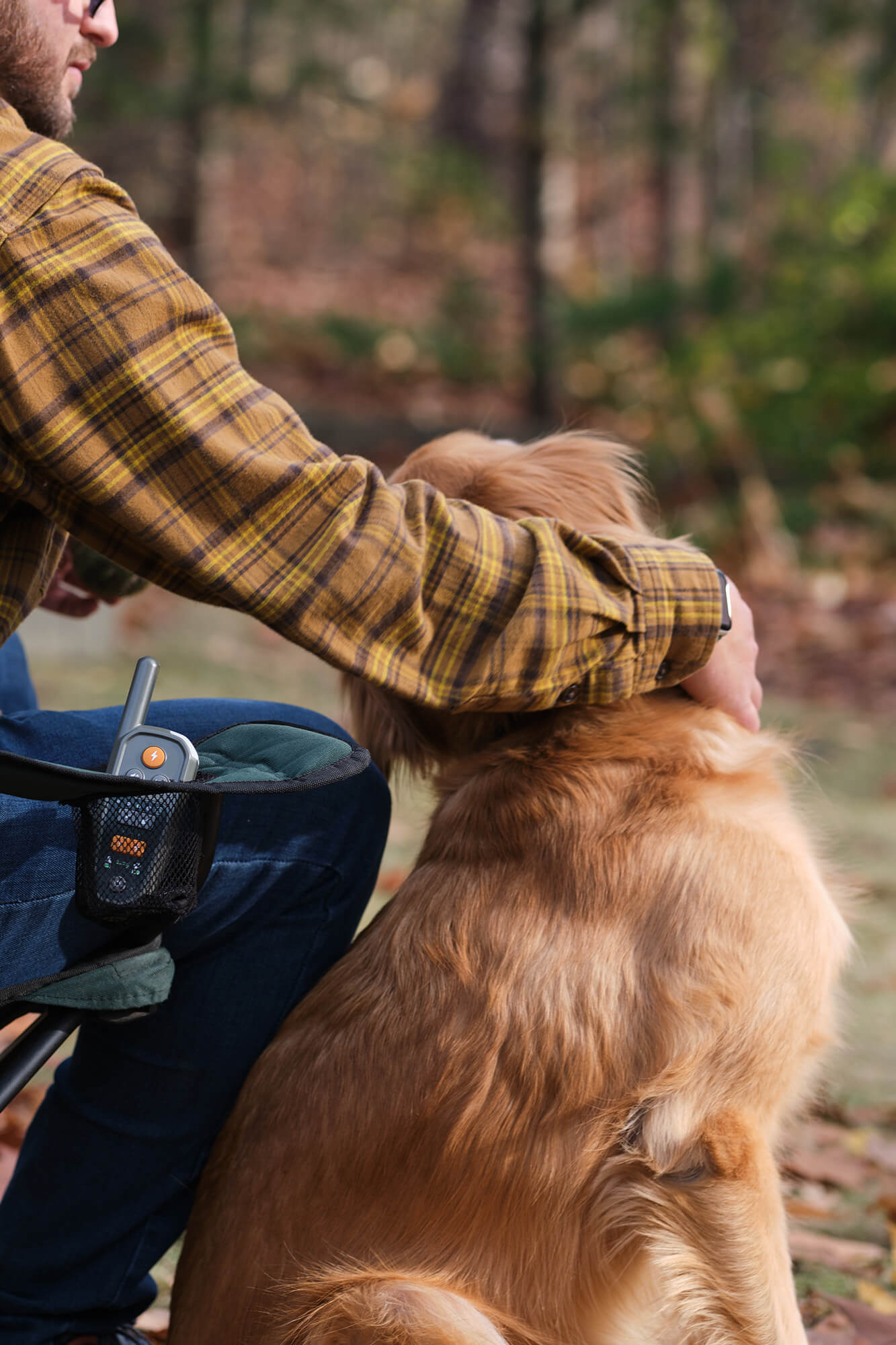Man petting a golden retriever while sitting in a camp chair with Heel™ Roam 350™ Remote resting in the cupholder
